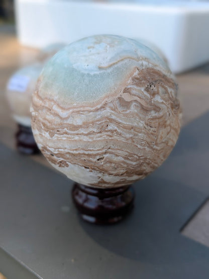 Front view of the 63mm Blue Aragonite sphere featuring a horizontal, unpolished vug running along the aragonite banding.