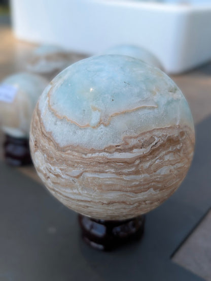Angled view of the 63mm Blue Aragonite sphere showing detailed, sweeping white and brown aragonite banding.