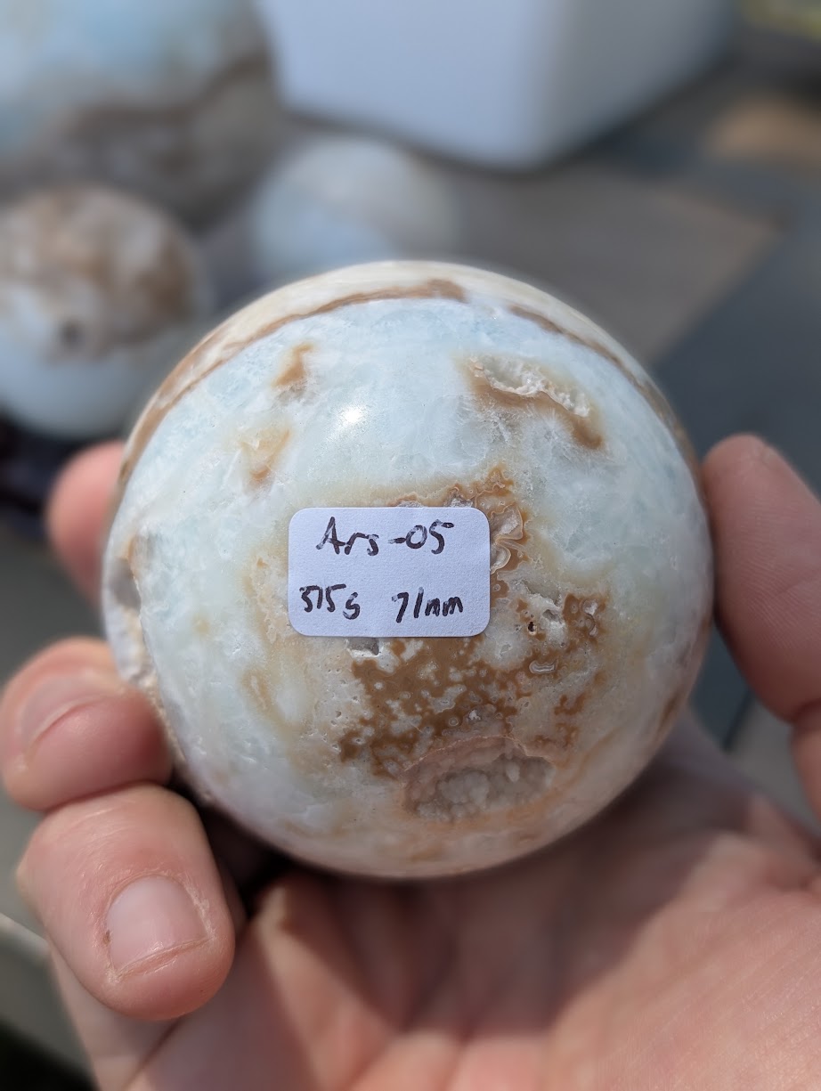 Base view of the 71mm Blue Aragonite sphere held in hand, showing the 515g weight label for variant Ars-05.