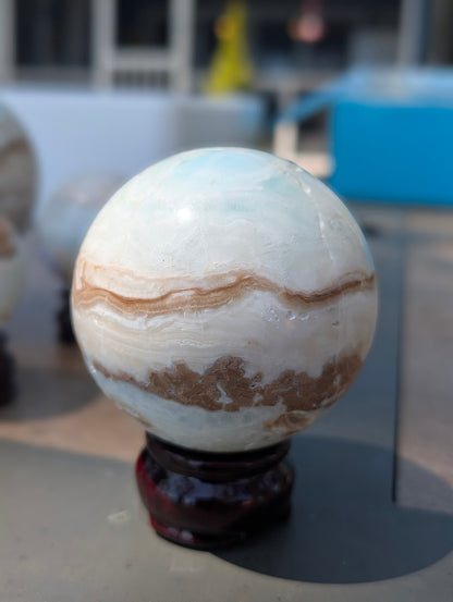 Front view of the exact 71mm Blue Aragonite and Caribbean Calcite sphere showing smooth sandy banding over pale blue calcite.