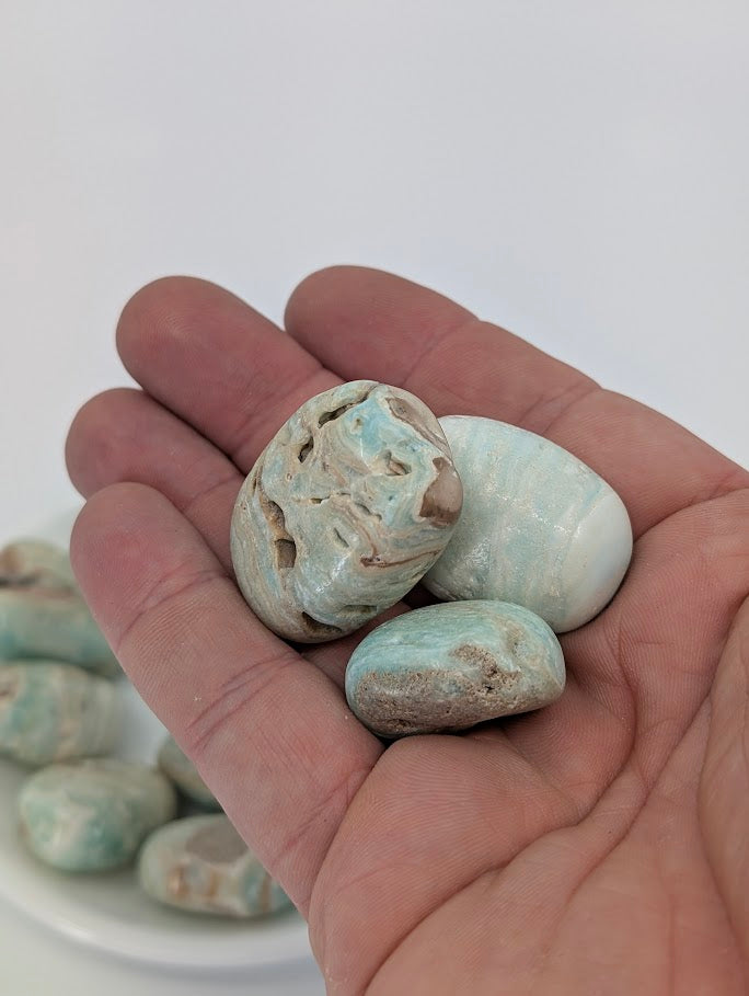 Hand holding Blue Aragonite tumbled stones highlighting natural patterning and smooth polish