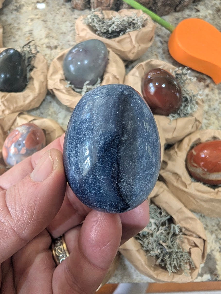 A 2-inch polished Blue Aventurine egg held in a hand, displaying a uniform soft blue natural stone surface with subtle mineral sparkle.