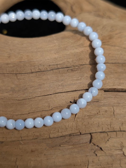 Macro view of polished 4mm Blue Lace Agate spherical beads on driftwood, highlighting the crisp white lace patterns within the translucent blue quartz.