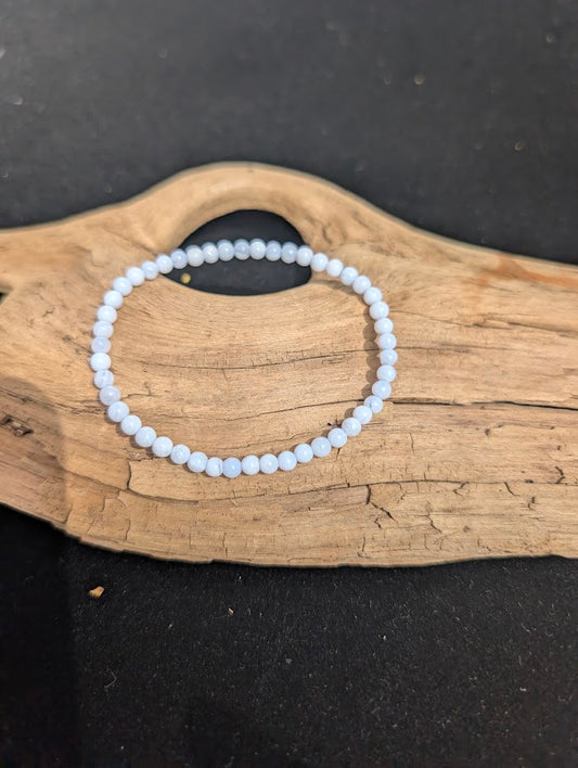 A 4mm Blue Lace Agate beaded bracelet resting on natural driftwood, displaying translucent pale blue and delicate white chalcedony banding.