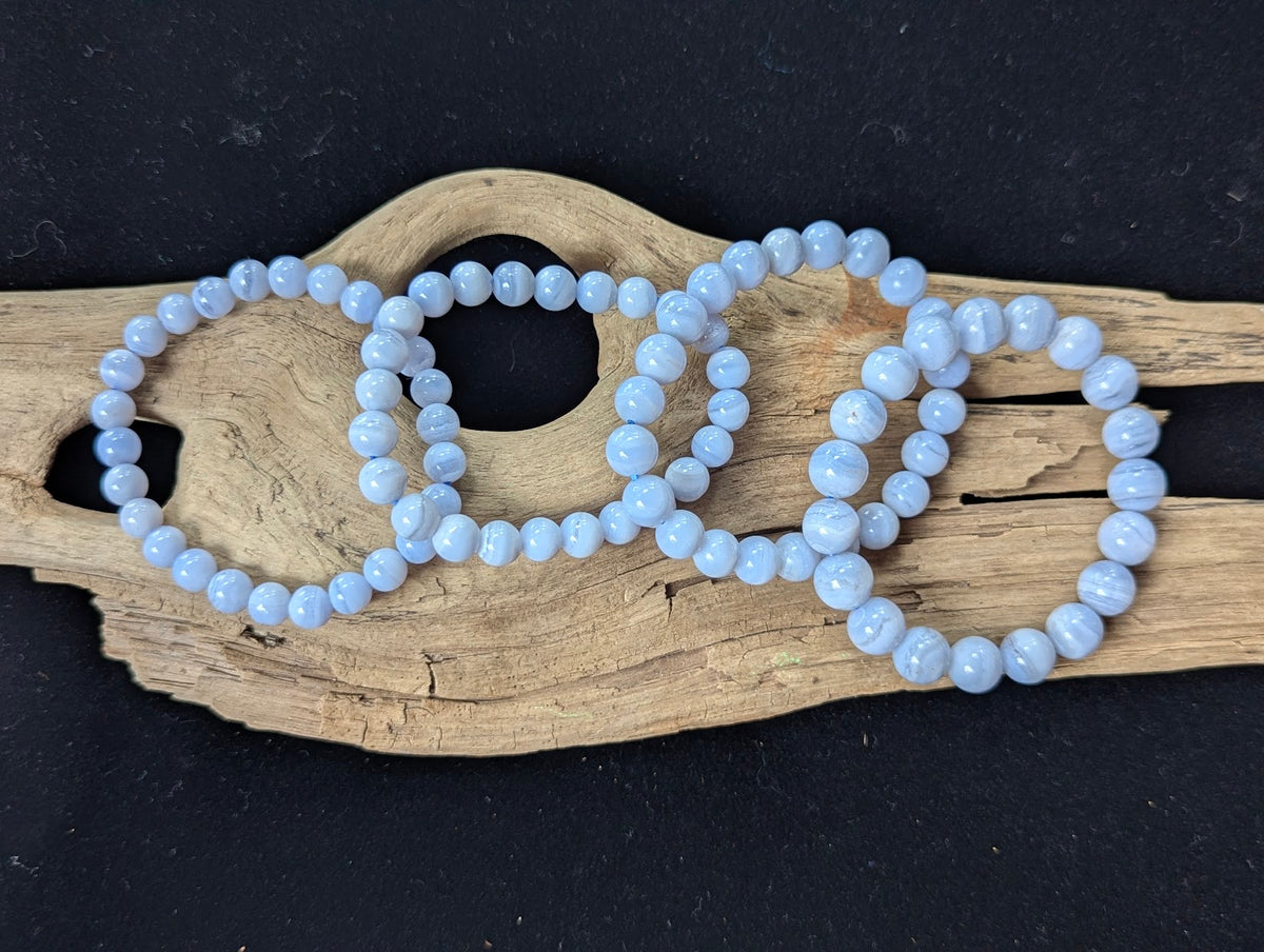 Four sizes of natural Blue Lace Agate bracelets from Namibia displayed on driftwood.