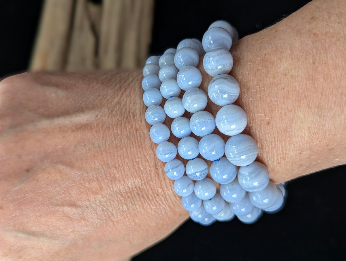 Stack of genuine Namibian Blue Lace Agate bracelets worn on a wrist, showing periwinkle blue colour and white banding.