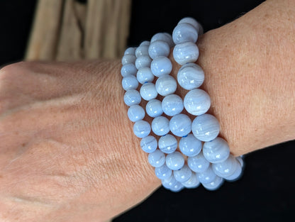 Stack of genuine Namibian Blue Lace Agate bracelets worn on a wrist, showing periwinkle blue colour and white banding.