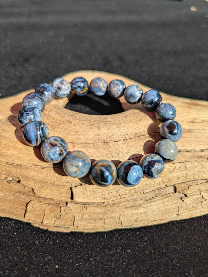 Intuitively selected 11mm AAA Grade Namibian Blue Pietersite beaded stretch bracelet displayed on driftwood, exhibiting strong midnight blue colouration.