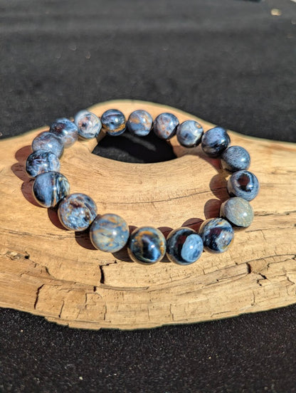 Intuitively selected 11mm AAA Grade Namibian Blue Pietersite beaded stretch bracelet displayed on driftwood, exhibiting strong midnight blue colouration.