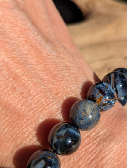 Macro close-up of an 11mm Blue Pietersite bracelet worn on a wrist, capturing the smooth spherical polish and optical iridescence.