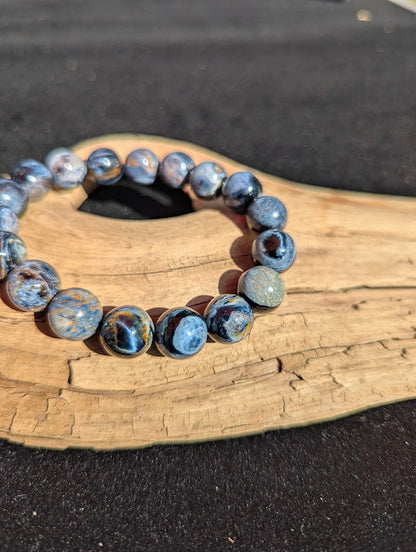 Macro close-up of an 11mm Blue Pietersite bracelet worn on a wrist, capturing the smooth spherical polish and optical iridescence.
