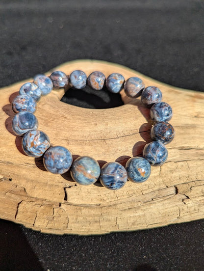 Intuitively selected 12mm AAA Grade Namibian Blue Pietersite beaded stretch bracelet on a driftwood display, showing multi-directional chatoyant flash.