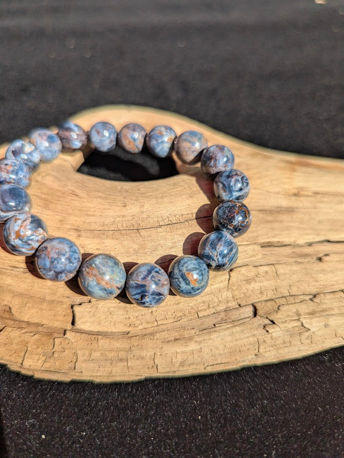 Macro detail of 12mm Blue Pietersite round beads highlighting the fractured and re-cemented silica matrix with golden rust inclusions.