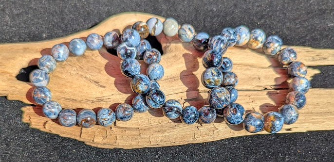 Suite of intuitively selected AAA Grade Namibian Blue Pietersite beaded stretch bracelets displayed together on driftwood, highlighting the multi-directional chatoyancy and brecciated matrix across different bead sizes.
