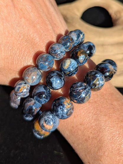 Stack of intuitively selected AAA Grade Namibian Blue Pietersite beaded bracelets worn together on a wrist, demonstrating size progression, high vitreous lustre, and deep blue chatoyant flashes.