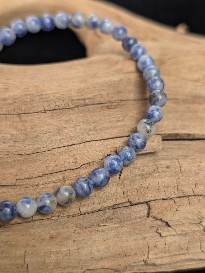 Macro view of polished 4mm Blue Point Jasper spherical beads on driftwood, highlighting the natural blue and white matrix of the stone.
