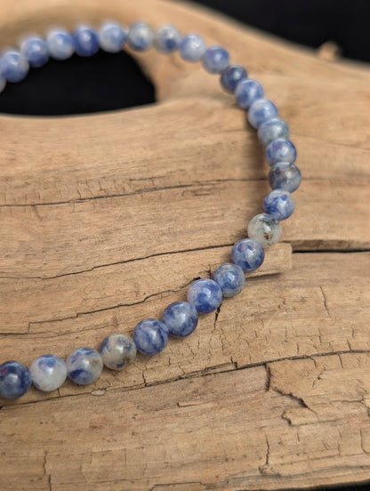 Macro view of polished 4mm Blue Point Jasper spherical beads on driftwood, highlighting the natural blue and white matrix of the stone.