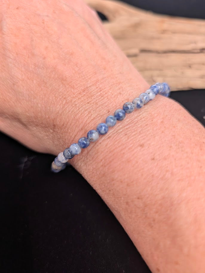 Natural sunlight on a 4mm blue and white Blue Point Jasper stretch bracelet worn on a wrist.