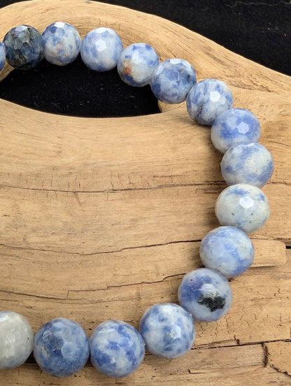 Macro close-up of 8mm faceted Blue Point Stone beads highlighting the geometric cut and the natural deep blue dumortierite inclusions within the quartz matrix.