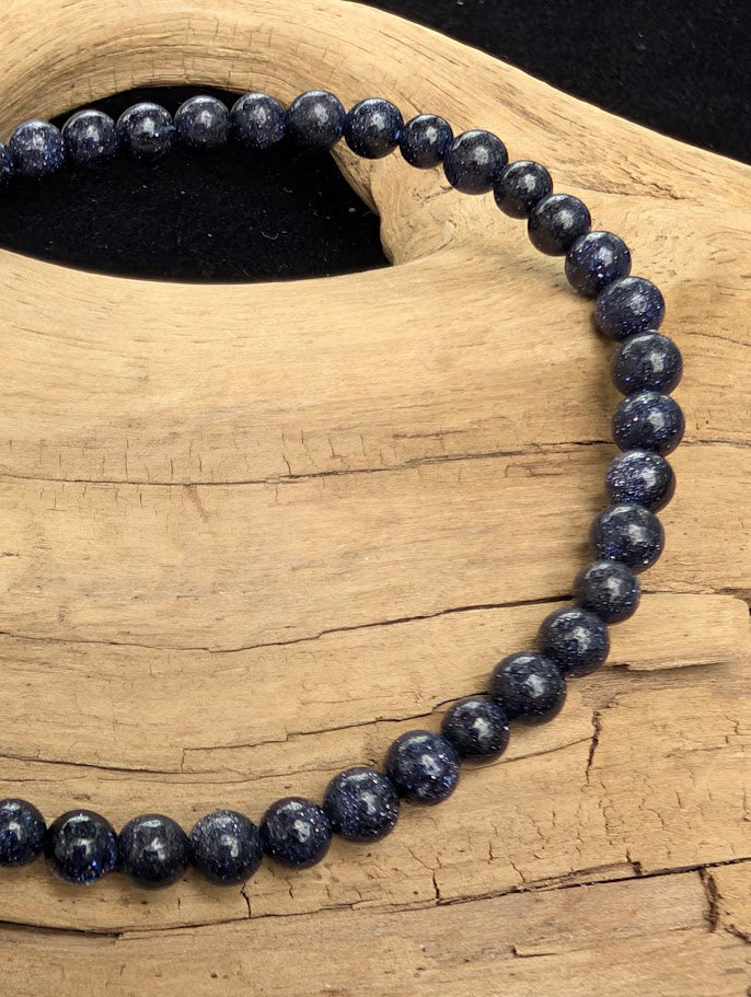 Macro close-up of 4mm polished Blue Sandstone beads highlighting the high-gloss finish and the metallic starry sparkle.
