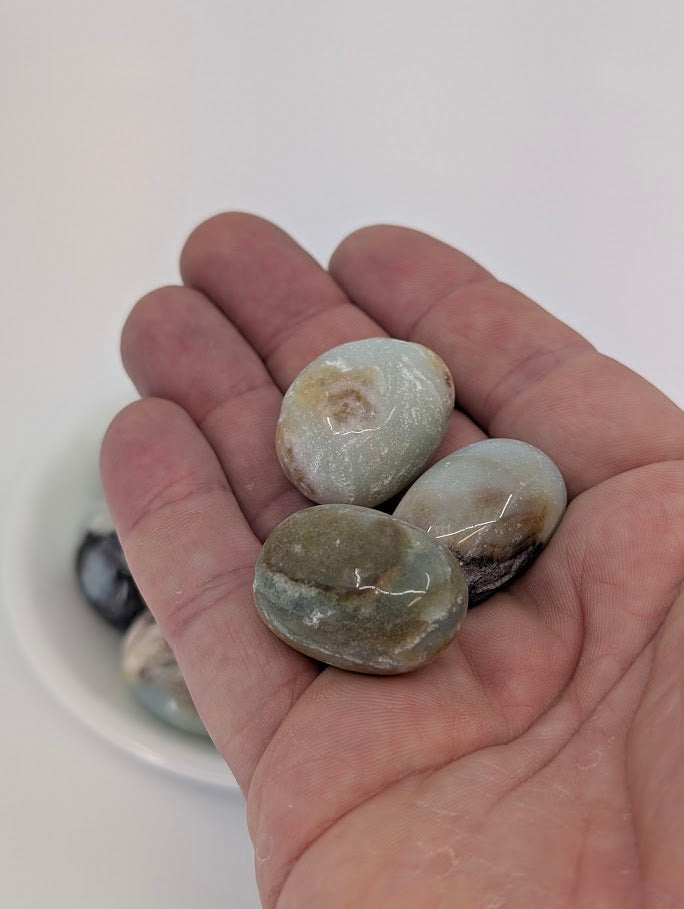 Hand holding Blue Sky Opal tumbled stones to show scale and finish