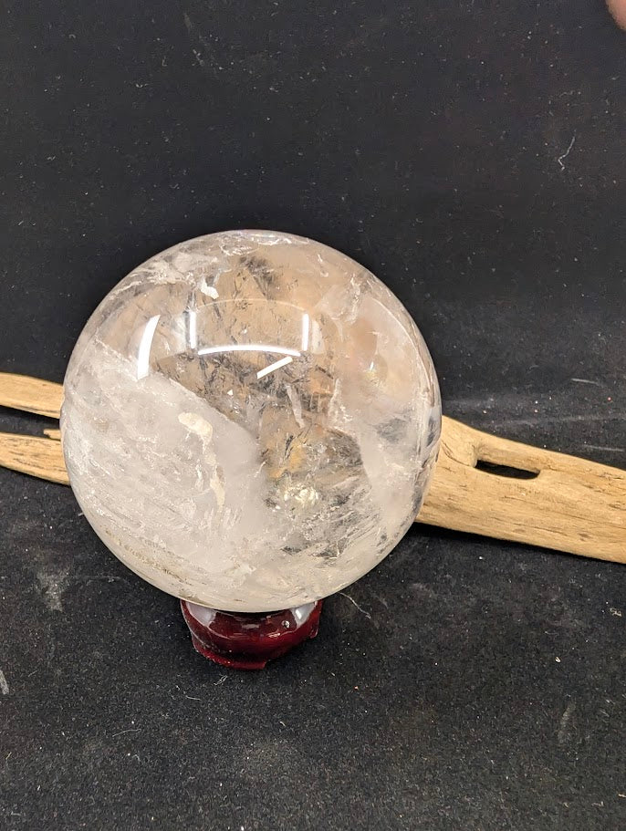 Angled view of a 1.12 kg Brazilian clear quartz enhydro sphere on a display stand, highlighting the large internal negative crystal cavity.