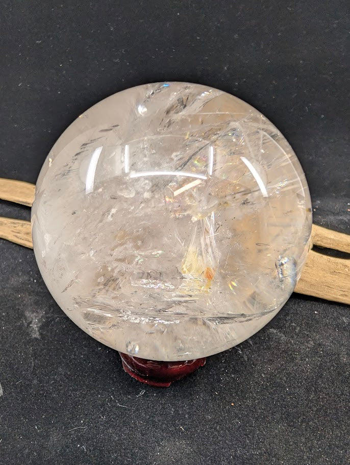 A 93mm Brazilian clear quartz enhydro sphere on a stand, clearly displaying vibrant internal rainbow iridescence and golden hematite inclusions.