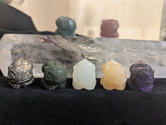 A group of hand-carved Bulbasaur Pokémon totems in various natural minerals.
