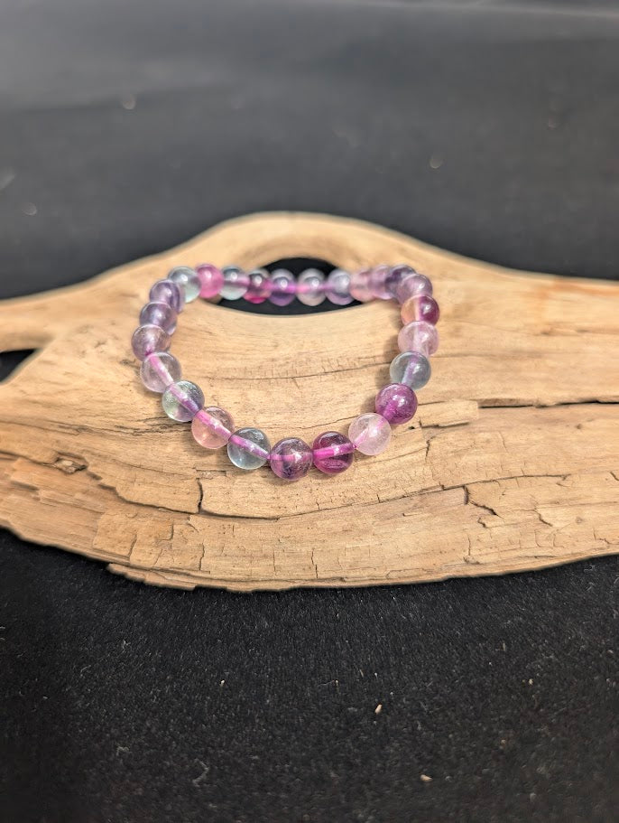 8mm Candy Fluorite beaded bracelet resting on a driftwood display, showing translucent purple and pink stones.