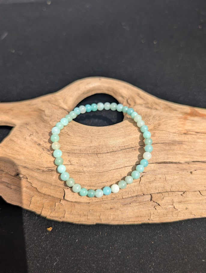 A 4mm Caribbean Calcite beaded bracelet resting on natural driftwood, displaying soft pastel blue and creamy white colors.