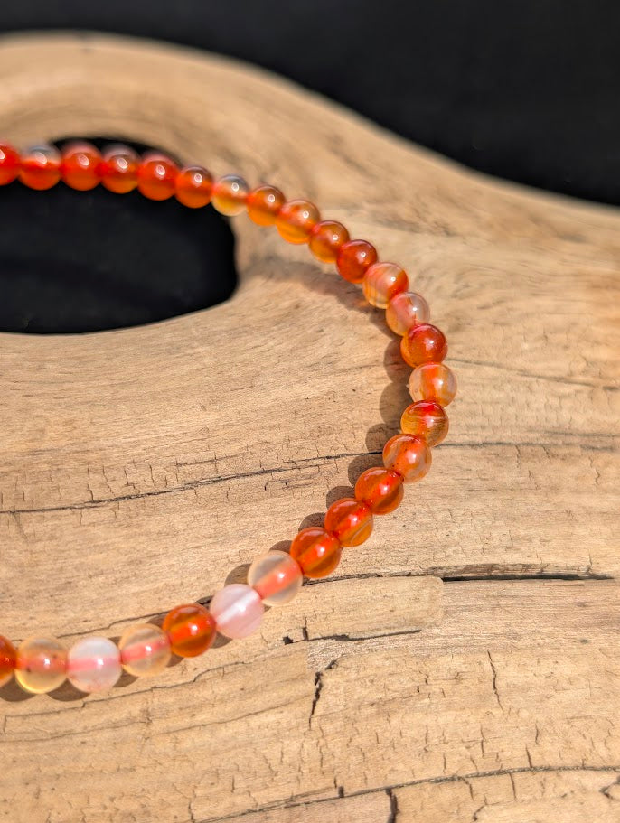 Macro view of polished 4mm Carnelian spherical beads on driftwood, highlighting the natural, un-dyed colour zoning of the chalcedony.