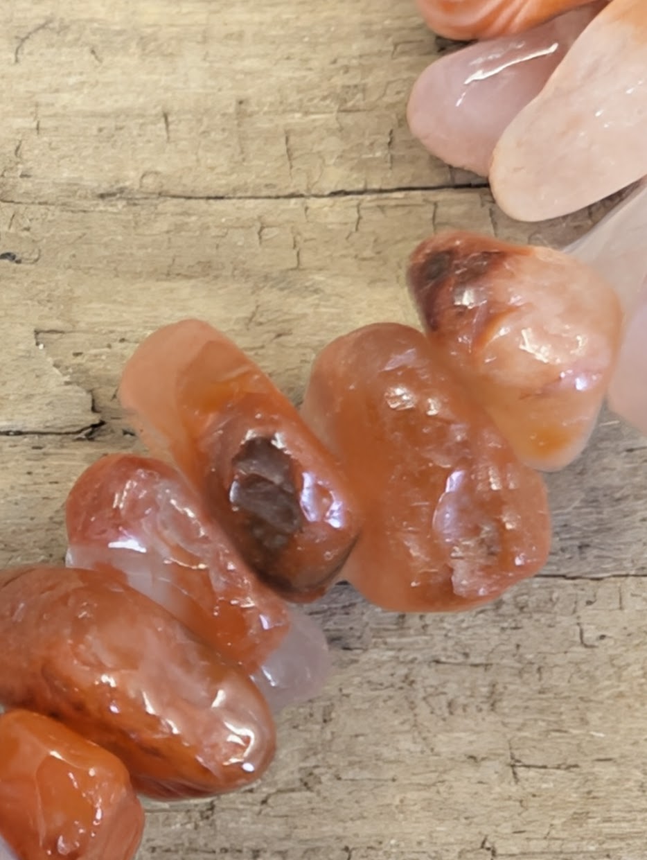 Extreme macro shot of tumbled Carnelian crystal chips, showcasing the smooth, high-gloss finish and unique internal patterns of each stone.
