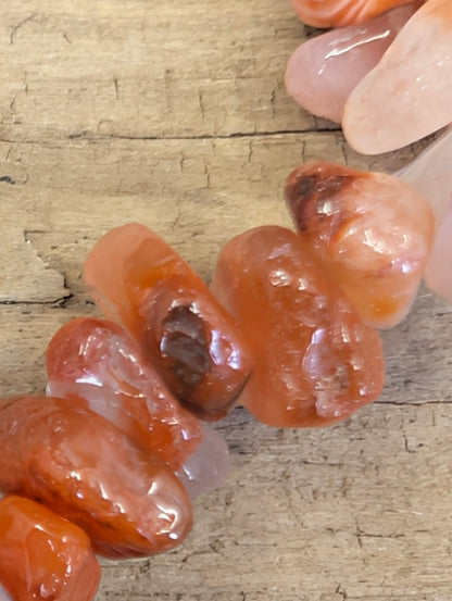 Extreme macro shot of tumbled Carnelian crystal chips, showcasing the smooth, high-gloss finish and unique internal patterns of each stone.