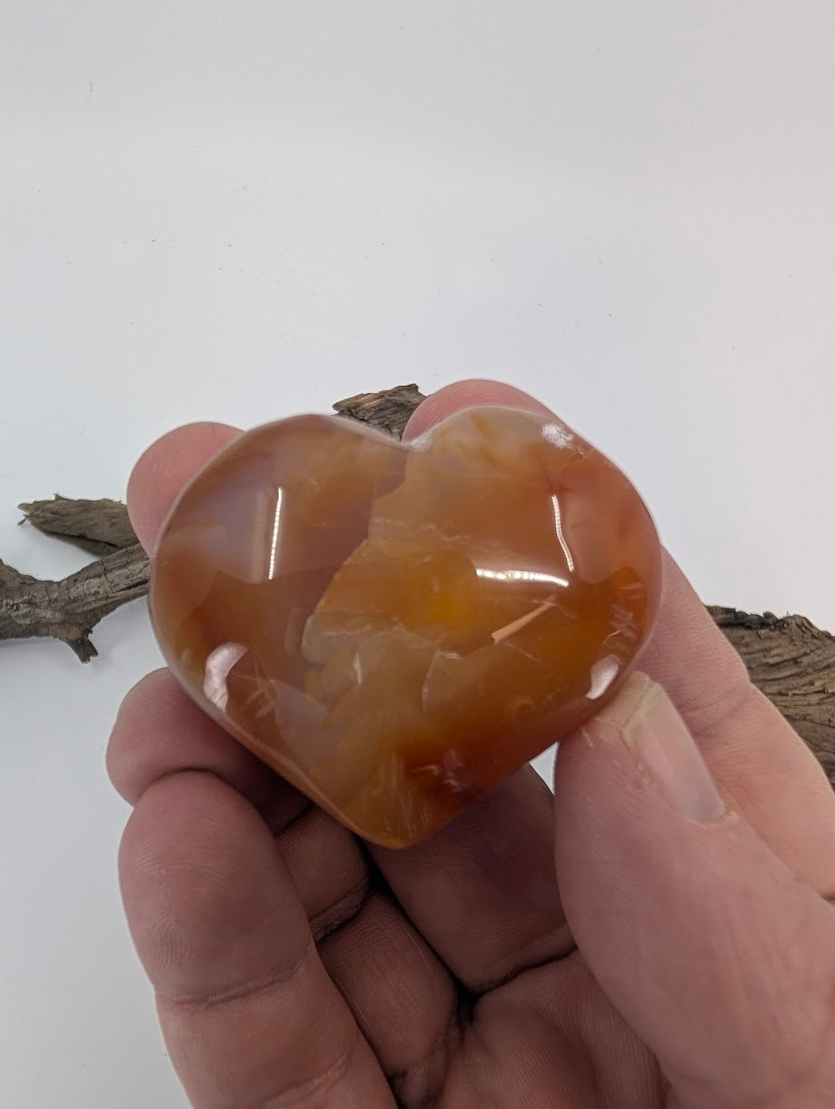 Hand holding an 80g Carnelian heart showing translucency and polish.