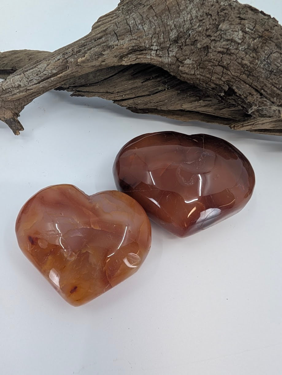 Pair of Carnelian hearts showing deep reddish-orange color on driftwood.