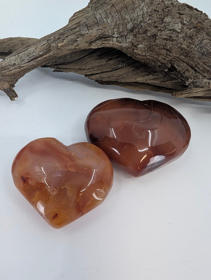 Pair of Carnelian hearts showing deep reddish-orange color on driftwood.