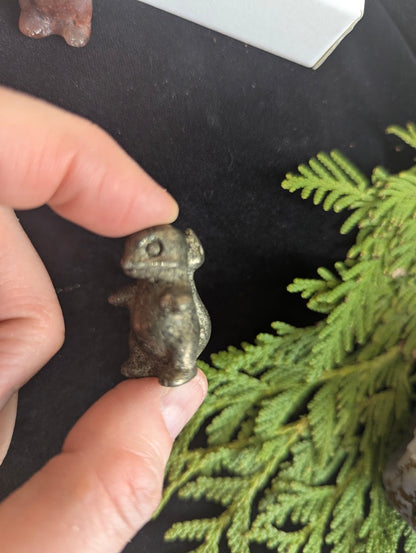 Side view of a 3cm Charmeleon carved from metallic Pyrite held in hand.