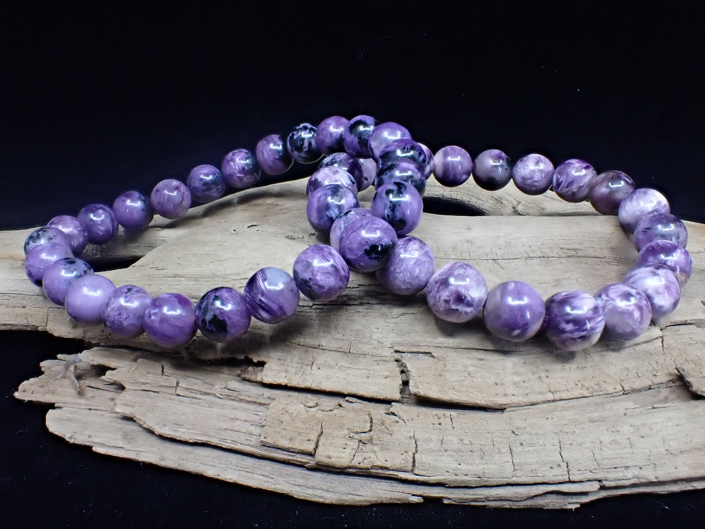 Two high-quality Charoite bracelets displayed on driftwood to highlight natural polish.