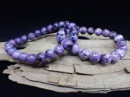 Two high-quality Charoite bracelets displayed on driftwood to highlight natural polish.