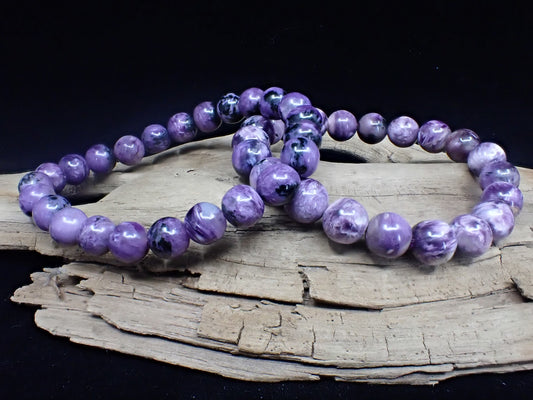 Two high-quality Charoite bracelets displayed on driftwood to highlight natural polish.
