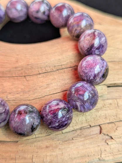 Macro close-up of a 13mm AAA Charoite beaded bracelet showing refined polish and distinct natural reddish Tinaksite inclusions within the purple matrix.