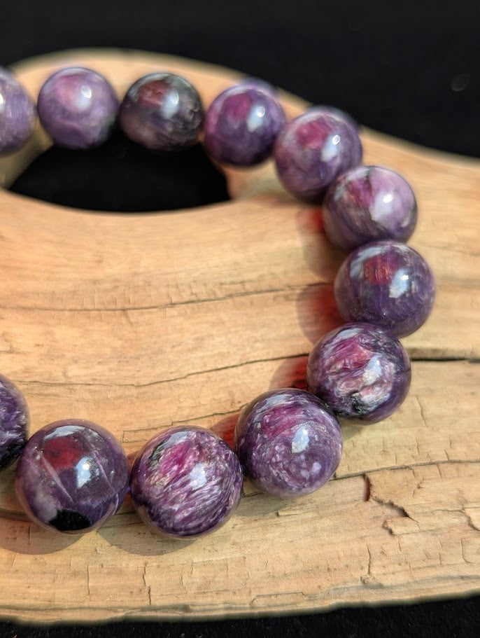 Macro close-up of a 14mm AAA Charoite beaded bracelet showing refined polish and distinct natural reddish Tinaksite inclusions within the purple matrix.