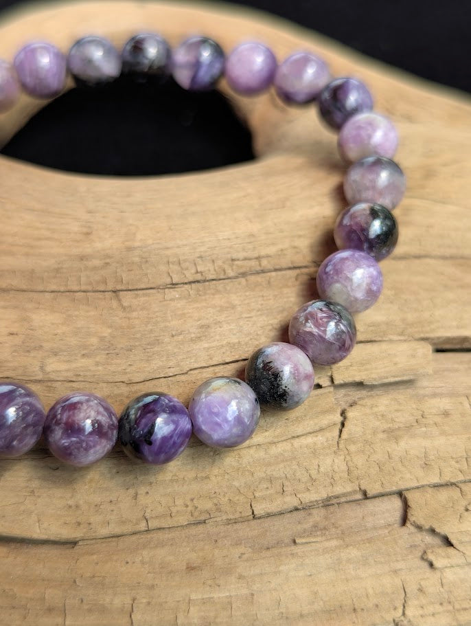 Macro close-up of a 7mm AAA Charoite beaded bracelet highlighting silky purple chatoyancy and natural black Aegirine inclusions.