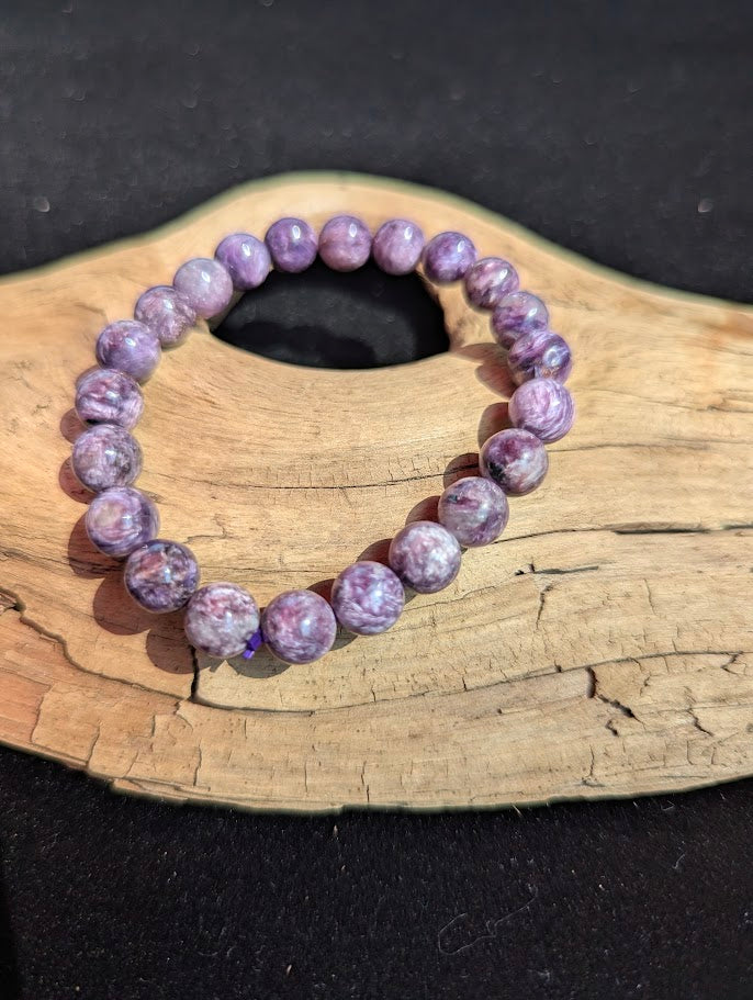 Intuitively selected 9mm AAA grade Siberian Charoite beaded stretch bracelet on a driftwood display, showing natural swirling purple matrix.