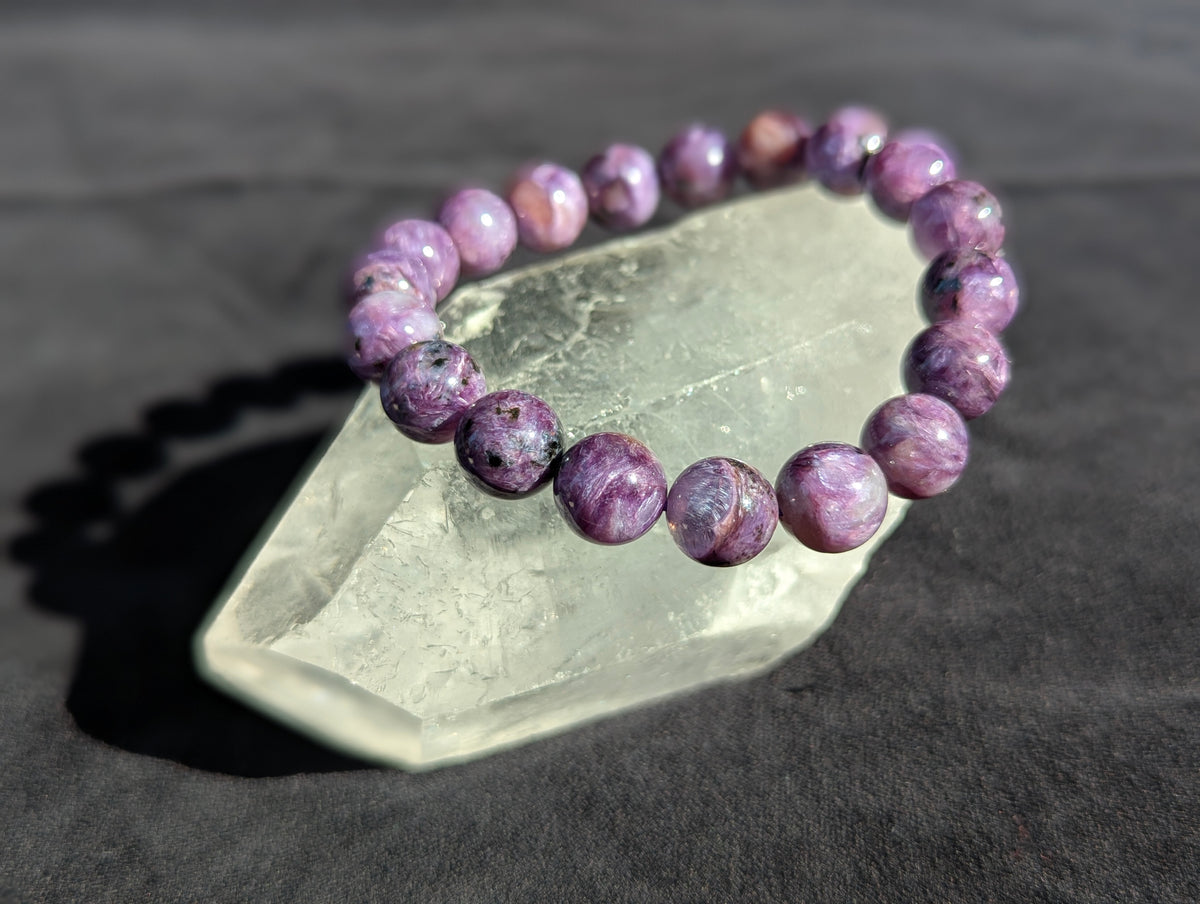 Intuitively selected AAA Museum Grade Siberian Charoite beaded stretch bracelet displayed resting on a natural clear quartz crystal point.