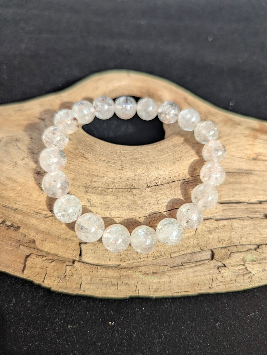 Intuitively selected 10mm AAA Grade Brazilian Cherry Blossom Garden Quartz beaded stretch bracelet on a driftwood display, showing water-clear quartz.