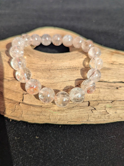 Intuitively selected 11mm AAA Grade Brazilian Cherry Blossom Garden Quartz beaded stretch bracelet resting on driftwood.