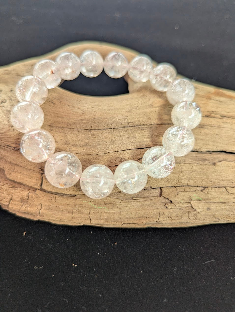 Intuitively selected 13mm AAA Grade Brazilian Cherry Blossom Garden Quartz beaded stretch bracelet resting on driftwood, showcasing large, pristine quartz spheres.