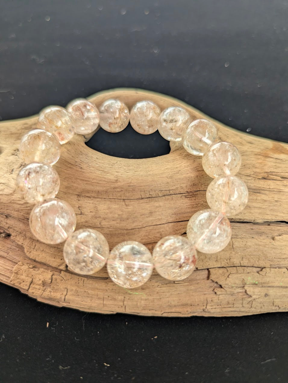 Intuitively selected 15mm AAA Grade Brazilian Cherry Blossom Garden Quartz beaded stretch bracelet on a driftwood display, showcasing highly transparent collector-grade quartz spheres.