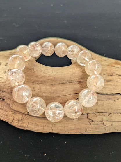 Intuitively selected 15mm AAA Grade Brazilian Cherry Blossom Garden Quartz beaded stretch bracelet on a driftwood display, showcasing highly transparent collector-grade quartz spheres.